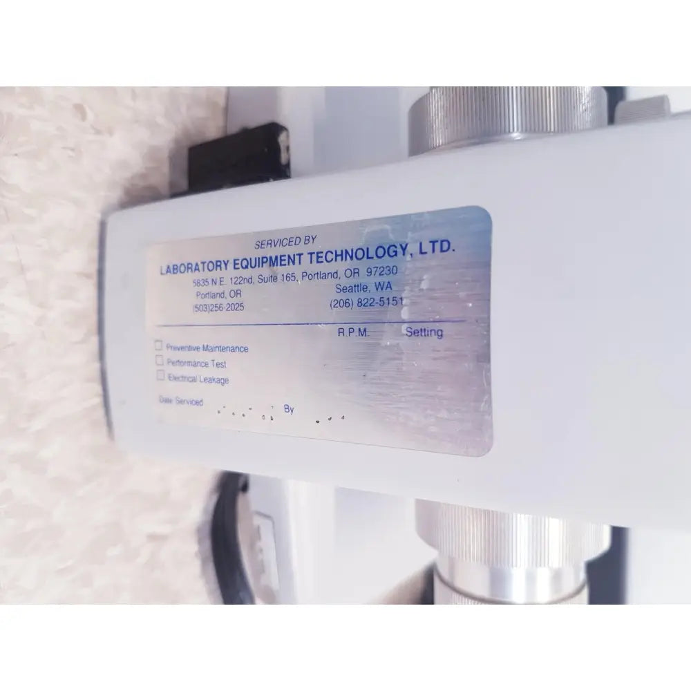 White rectangular service label with blue text and metallic sheen on AO scientific instruments one-ten illuminator model 1130A