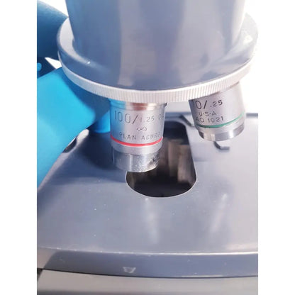Gray microscope with silver objective lenses marked 100/1.25 and 10/.25 mounted on AO Scientific Instruments One-Ten illuminator model 1130A