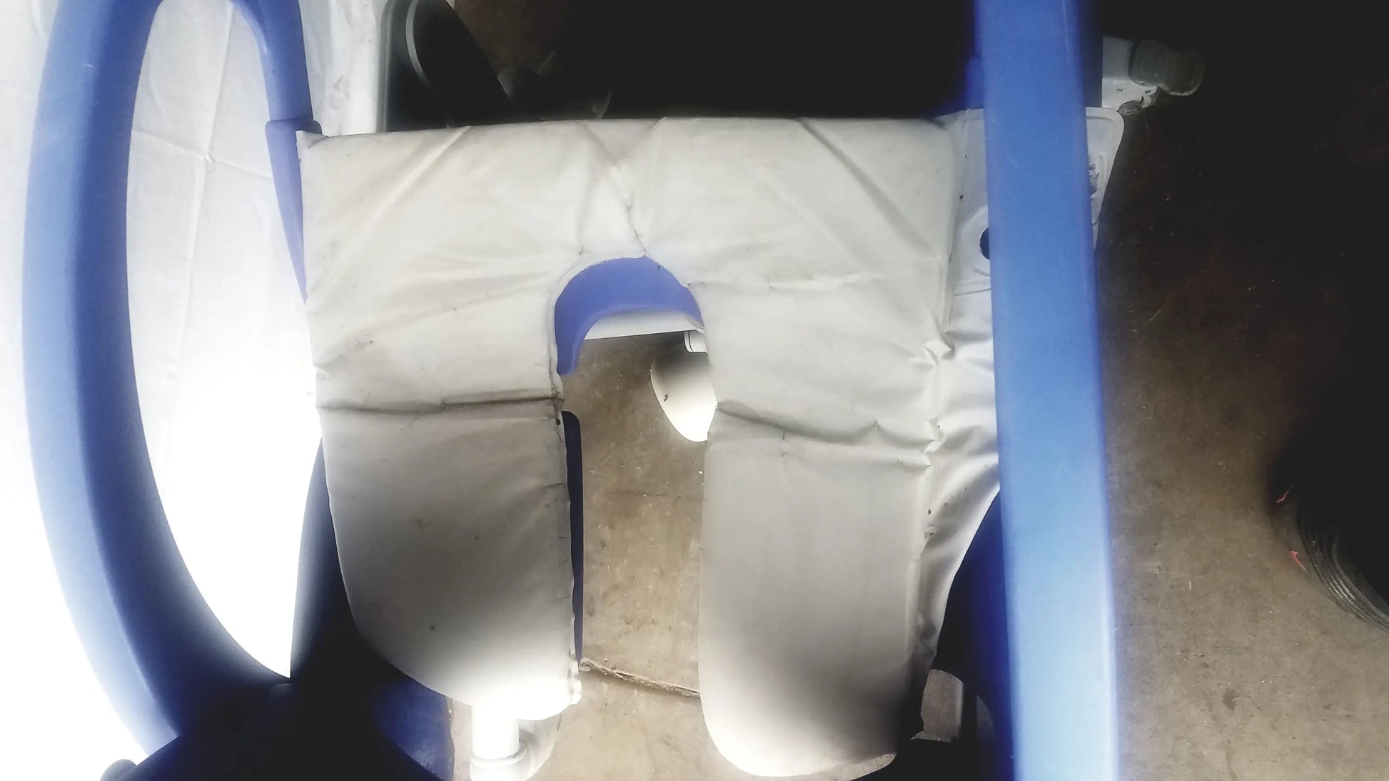 Blue plastic multipurpose hygiene chair with white padded seat and blue handlebars by Arjo Carendo