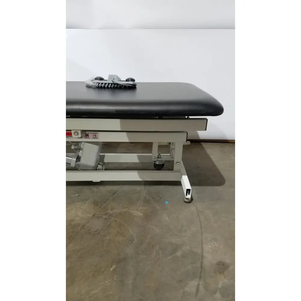 Armedica am-300 three section treatment table with black padded surface white metal frame and caster wheels