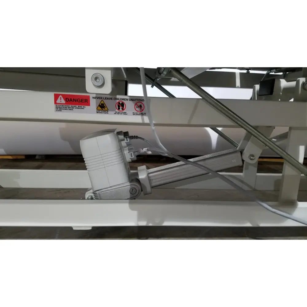 White electric lift mechanism with metallic arm and cables on the back side of armedica am 300 three section treatment table