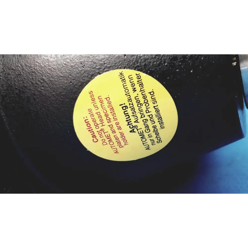 Yellow circular sticker with black and red text on dark surface of automet 2 variable speed grinder-polisher 120v
