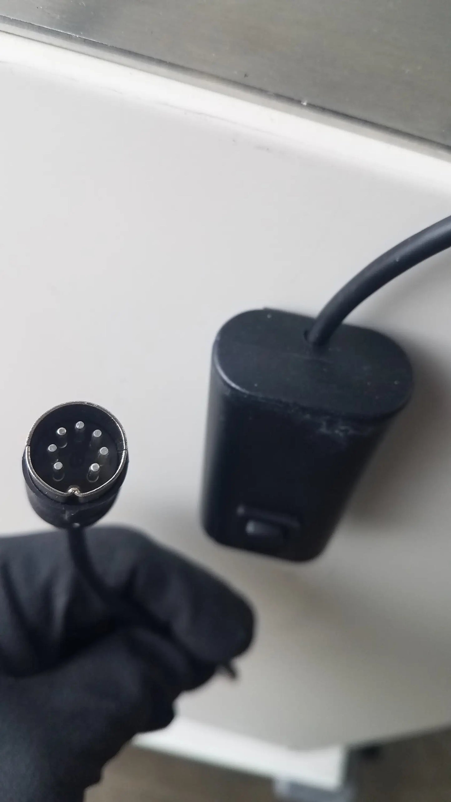 Black cylindrical connector with nine metallic pins held in a gloved hand for baker ss-600 positive pressure isolator