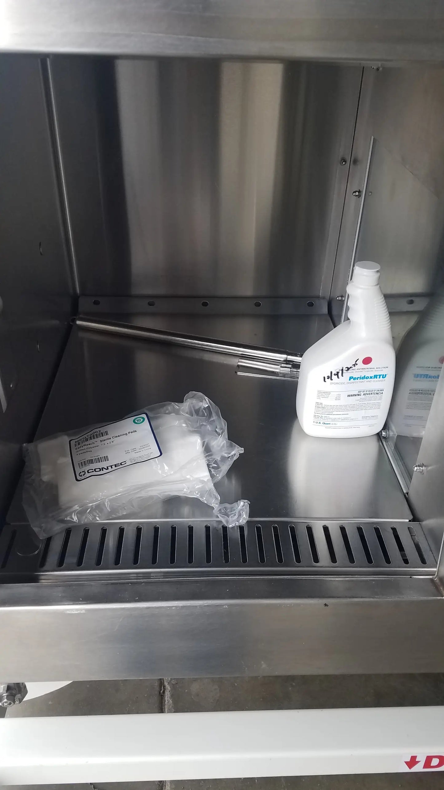 White plastic bottle of prohunt disinfectant spray with white cap on stainless steel shelf inside baker ss-600 sterilshield positive pressure isolator