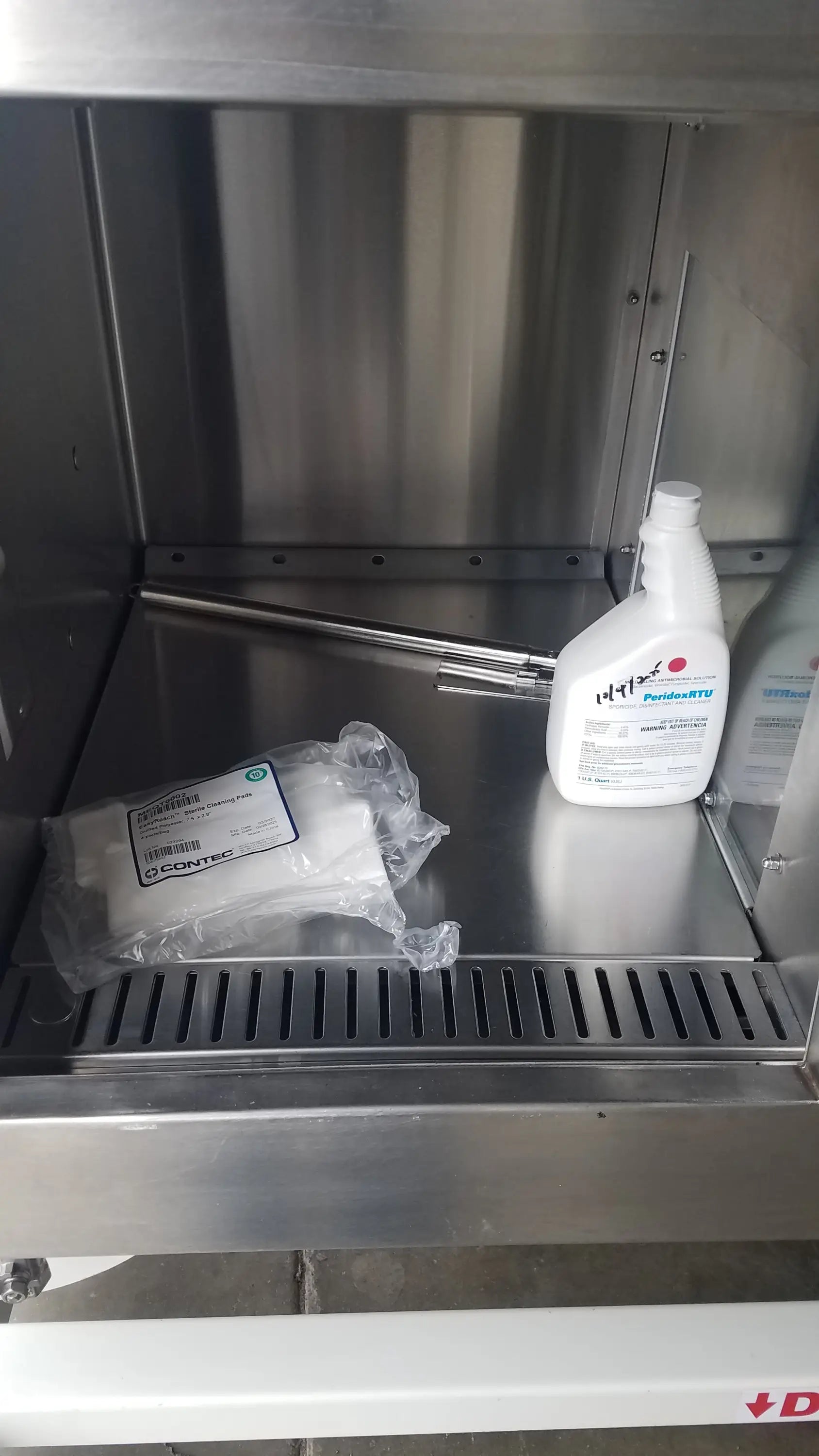 White plastic bottle of prohunt disinfectant spray with white cap on stainless steel shelf inside baker ss-600 sterilshield positive pressure isolator