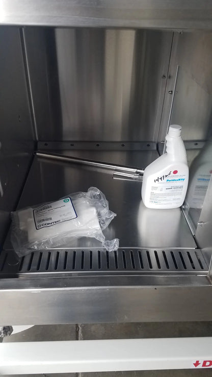White plastic bottle of prohunt disinfectant spray with white cap on stainless steel shelf inside baker ss-600 sterilshield positive pressure isolator