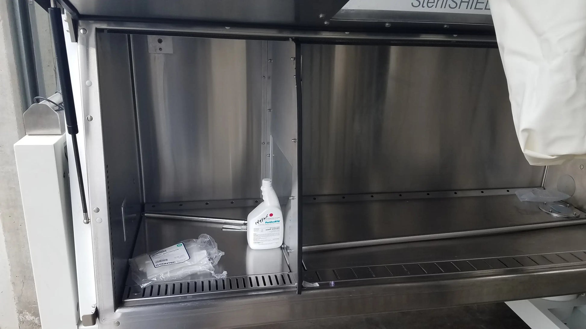 White spray bottle with green and red labeling inside stainless steel baker ss-600 sterilshield positive pressure isolator