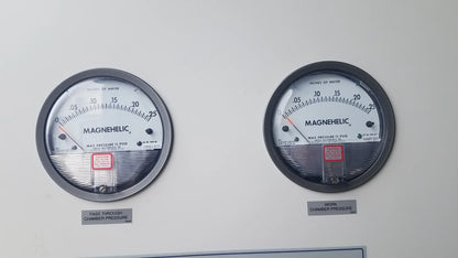Two black-rimmed pressure gauges with white faces and red needles on baker SS-600 sterilshield positive pressure isolator