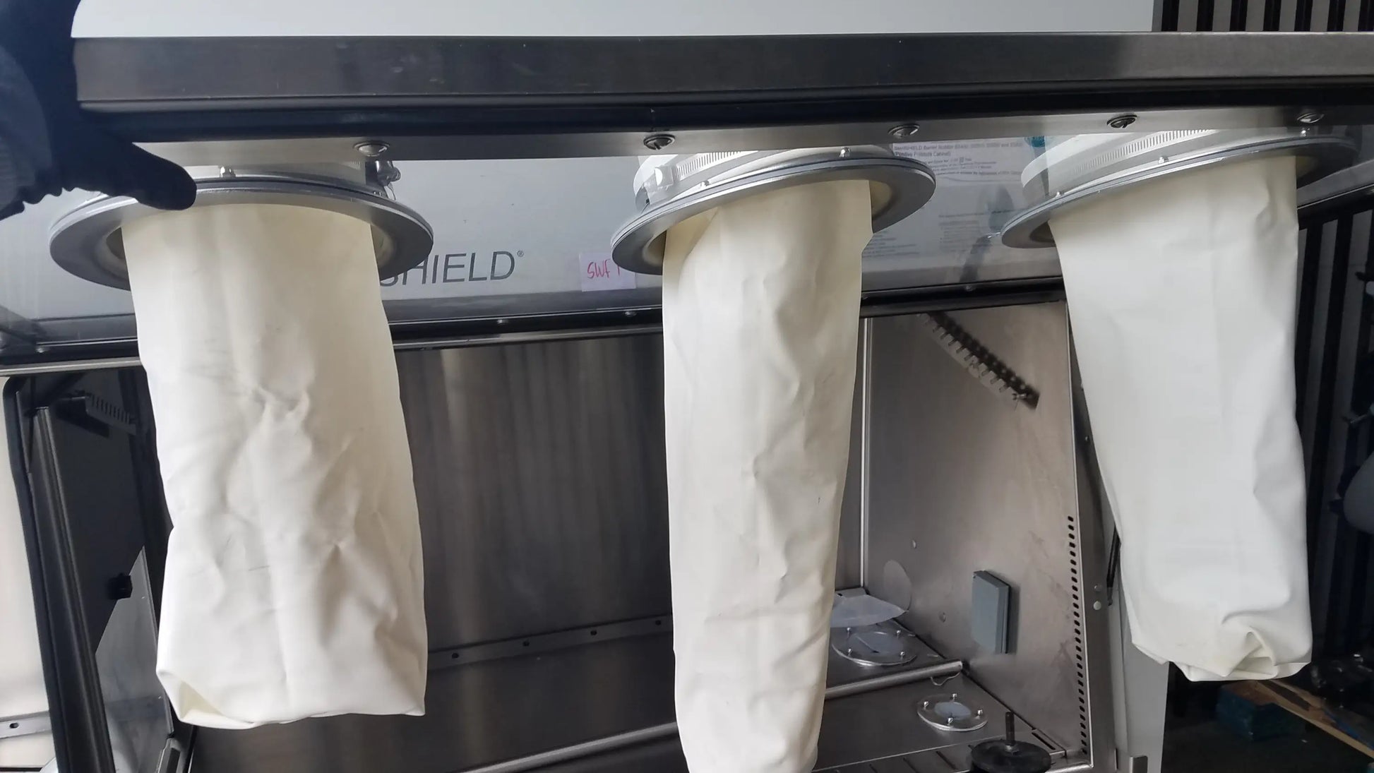 Three white cylindrical filter bags with metallic rims hang on baker ss-600 sterilshield positive pressure isolator