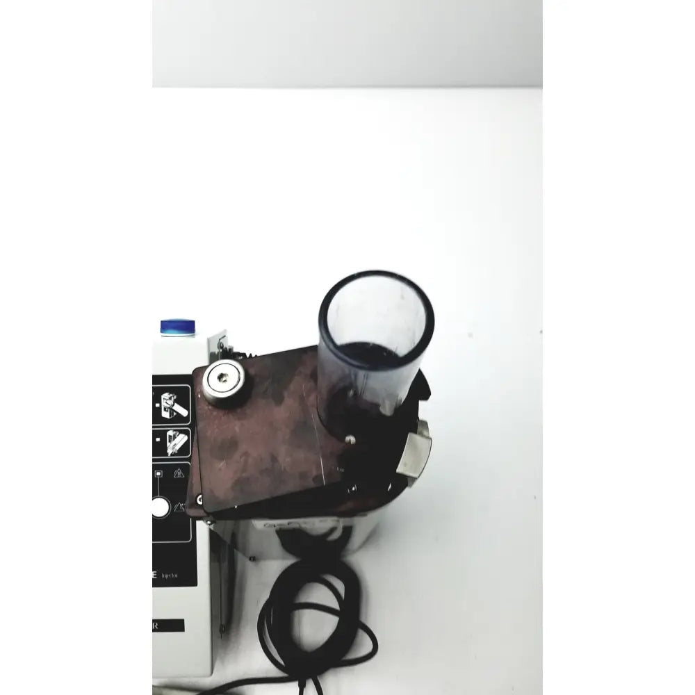 A transparent cylindrical container with black rim filled with dark liquid on metallic bard peripheral flowmate injector crosser in100