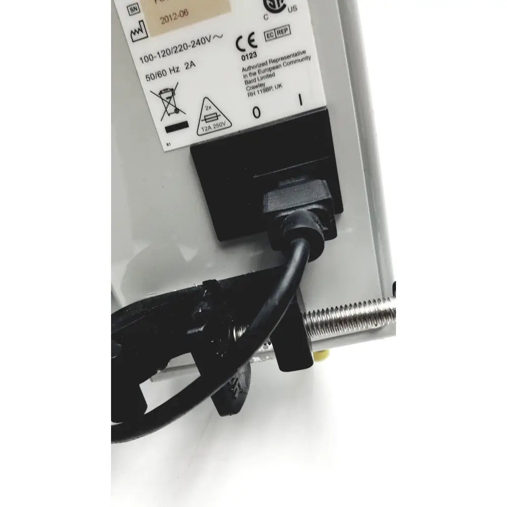 Black power cord plugged into a black electrical outlet on the back of a white bard peripheral flowmate injector crosser in100