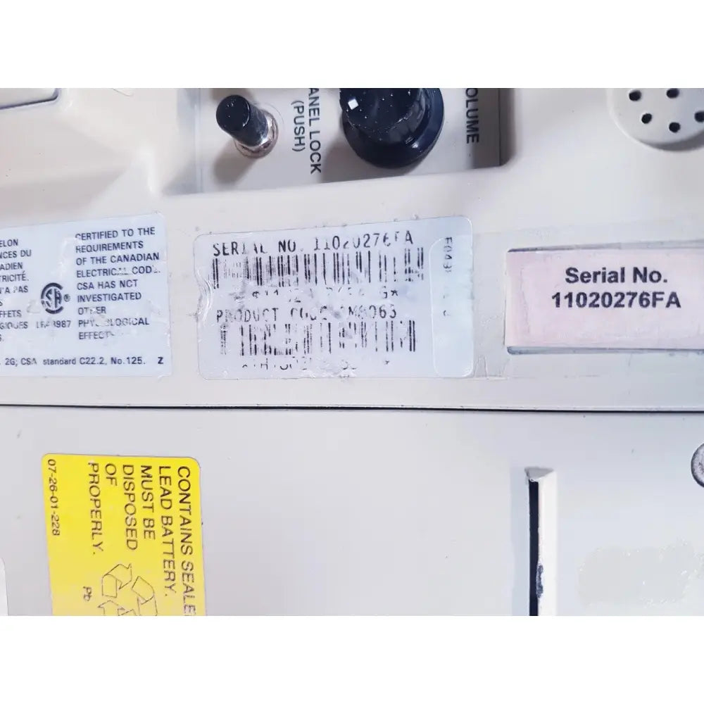 White plastic label with black text and barcode showing serial number 11020276fa on baxter 2m8063 volumetric infusiion pump