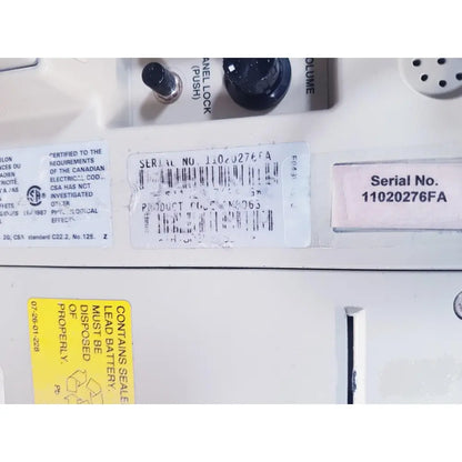 White plastic label with black text and barcode showing serial number 11020276fa on baxter 2m8063 volumetric infusiion pump