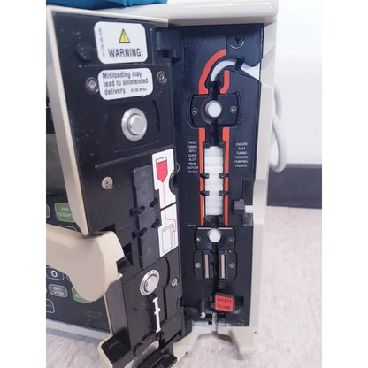 Black and beige baxter 2m8063 volumetric infusiion pump with orange tubing guide safety clamp and warning labels