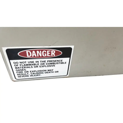 A rectangular danger warning label with black text on white background affixed to a gray surface of baxter scientific h2025-1a heater