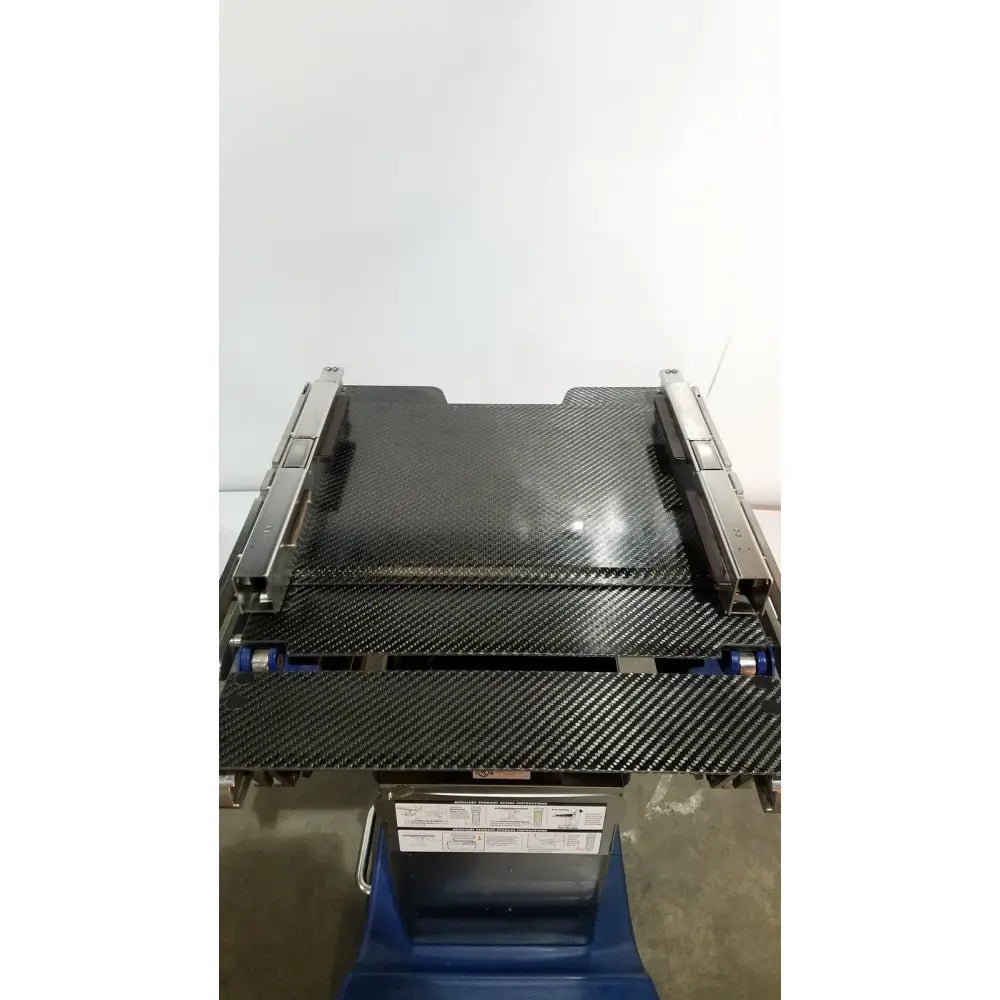 Black carbon fiber conveyor belt with metallic side rails and blue rollers on berchtold d850 operon surgical table