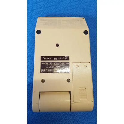 Beige plastic Bio-Dynamics Accu-Chek bG blood glucose monitor showing serial number label and paper roll slot