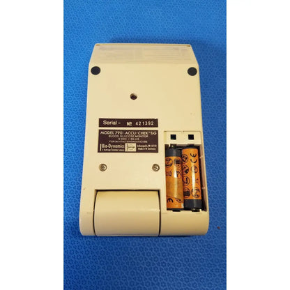 Cream-colored plastic bio-dynamics accu-chek bg blood glucose monitor with two orange and black batteries inserted