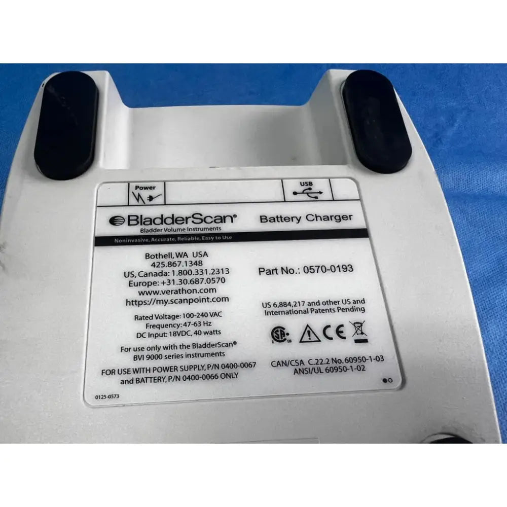 White plastic bladderscan battery charger with black rubberized footpads and detailed specification label for reuse medical use