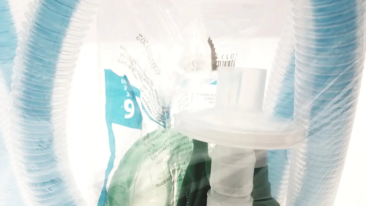 A clear plastic bag containing a white breathing circuit with blue tubing and printed labels breathing bag coaxial device