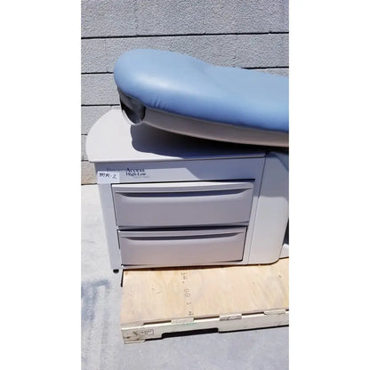 Light blue padded brewer access high-low exam table with gray metal base and two drawers for medical use