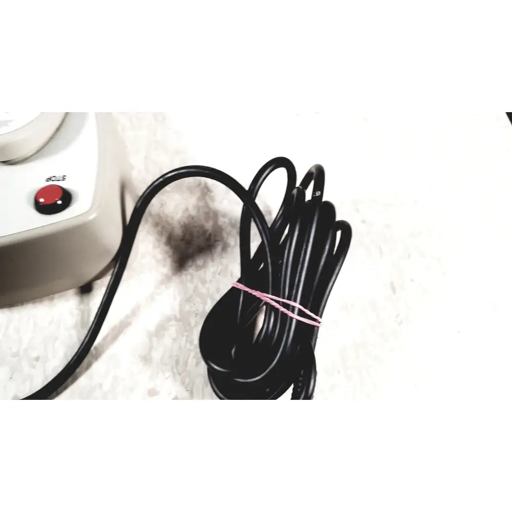 Black coiled power cord with pink tie beside white brewer high low power exam foot pedal for low power exam use