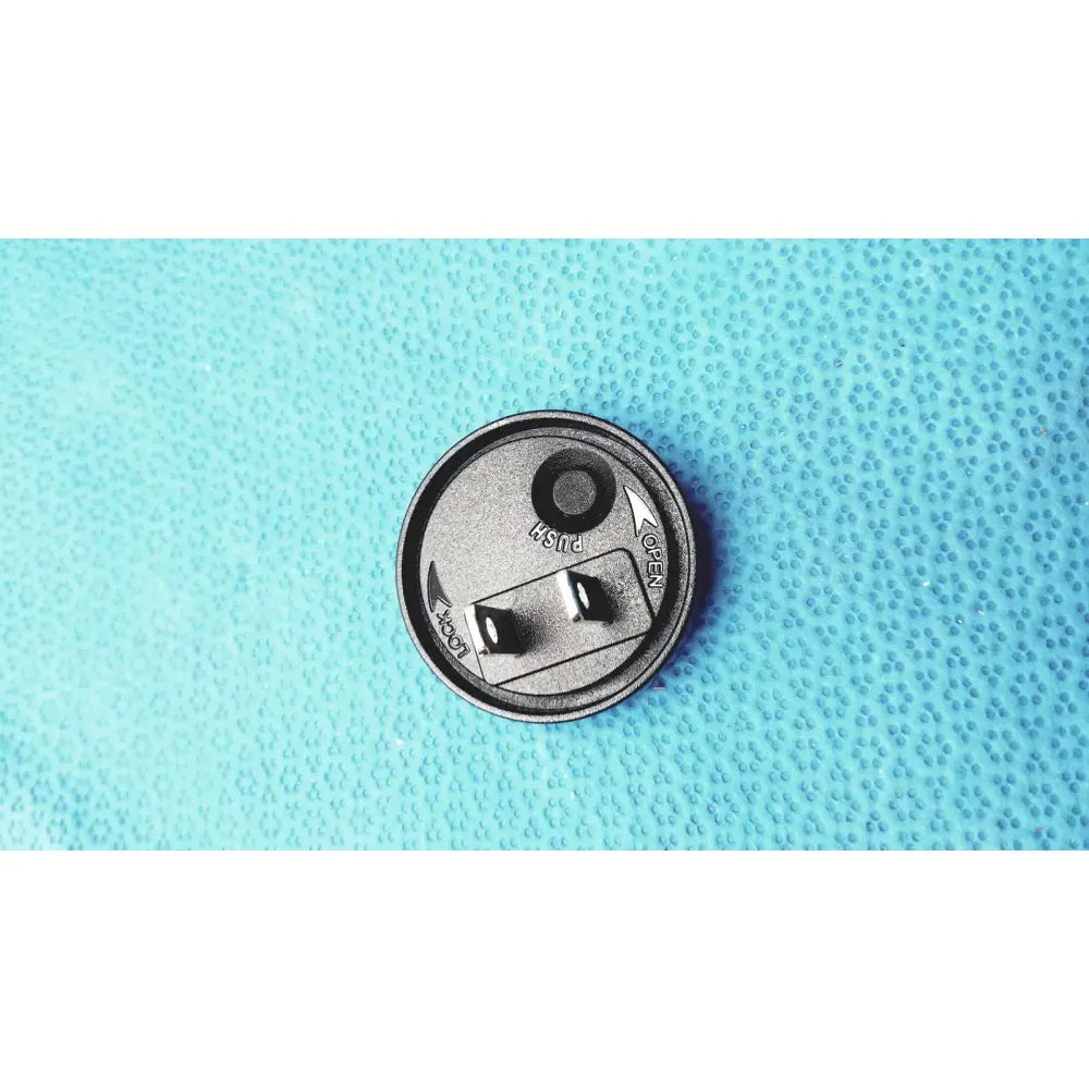 Silver-colored circular canister with textured surface and embossed push and open markings for burton ultraviolet examining light