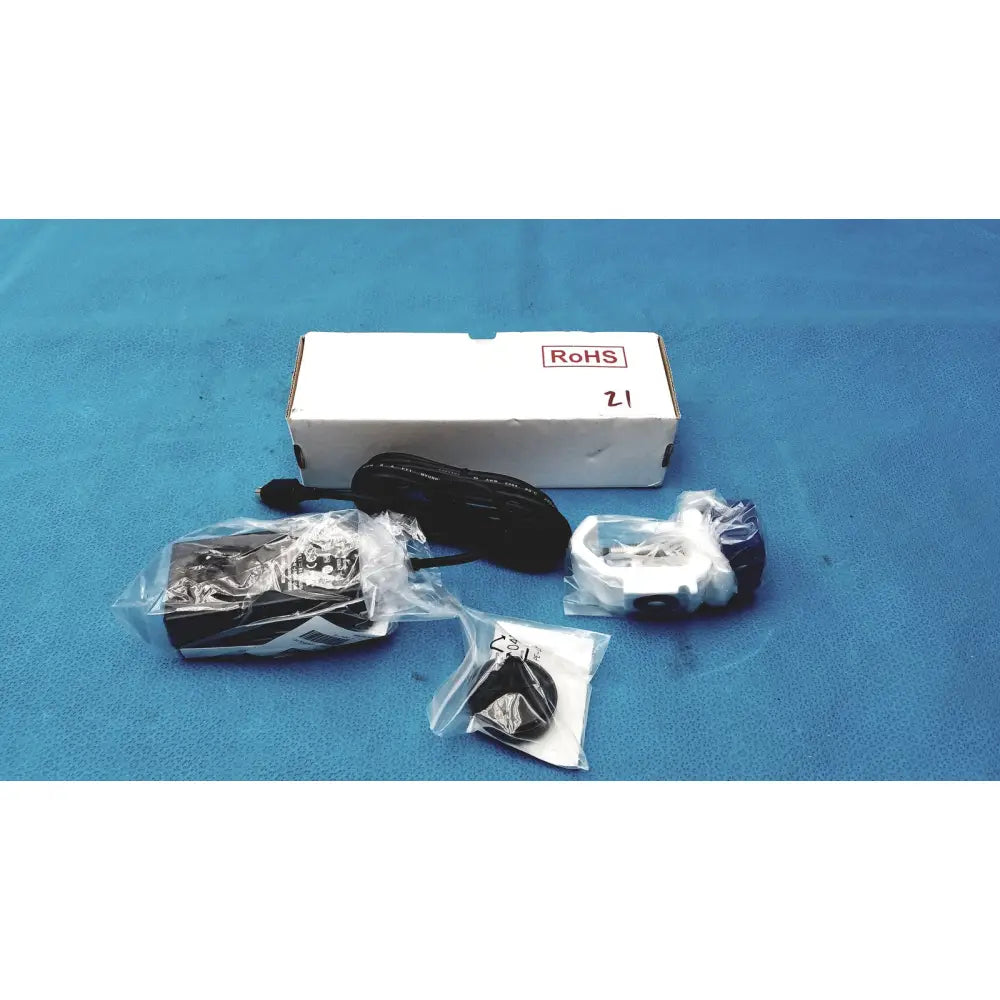 Black power adapter and cable in plastic packaging next to white burton ultraviolet examining light with black accents