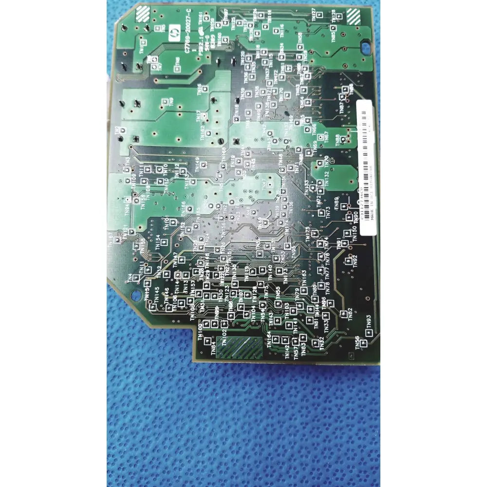 Green printed circuit board with black solder pads and silver traces featuring white barcode label for c7769-60007 carriage pca board