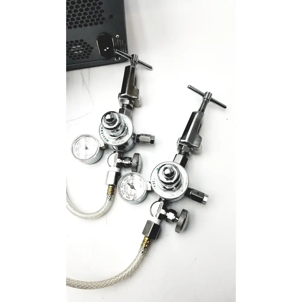 Two chrome-finished western medical gas regulators with pressure gauges and braided hoses on carefusion vmax encore analyzer