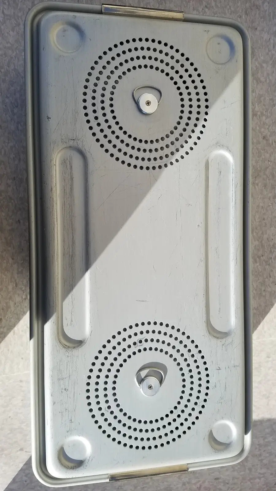 Silver metallic rectangular speaker grille with two circular perforations and integrated handles for case medical storage container
