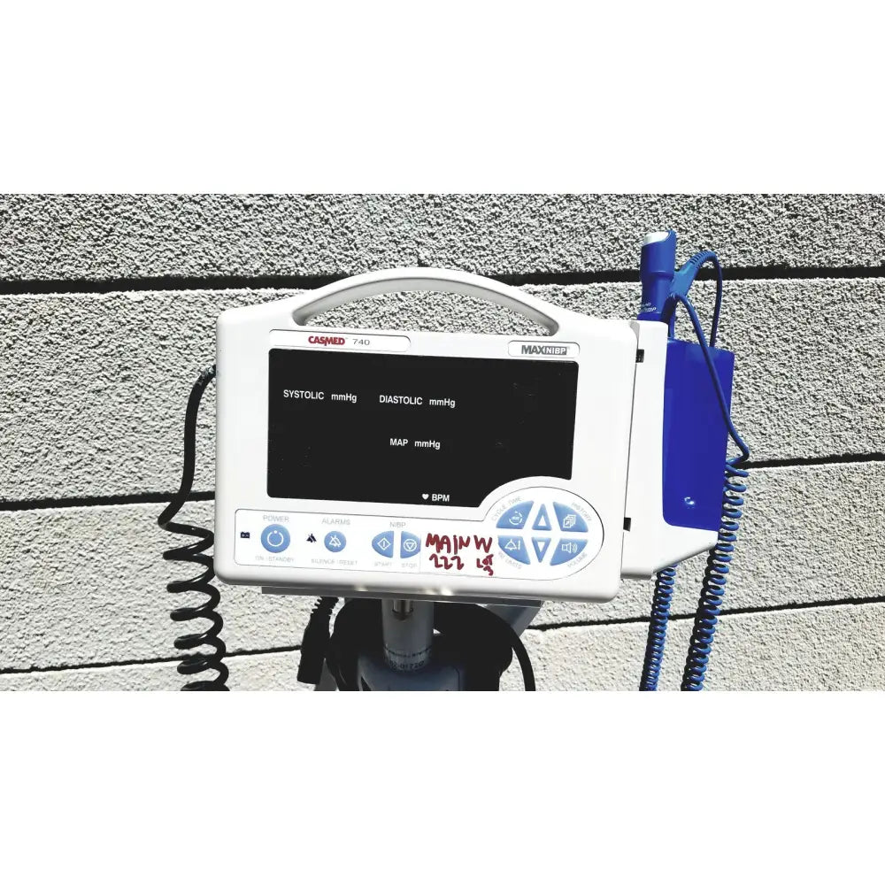 White casmed 740 vital signs monitor with black screen displaying blood pressure and blue coiled cables on rolling stand