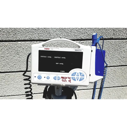 White casmed 740 vital signs monitor with black screen displaying blood pressure and blue coiled cables on rolling stand