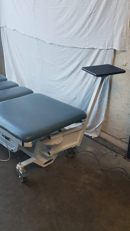 Gray padded Chattanooga triton dts traction table with black adjustable tray and white metal frame on casters for physical therapy equipment