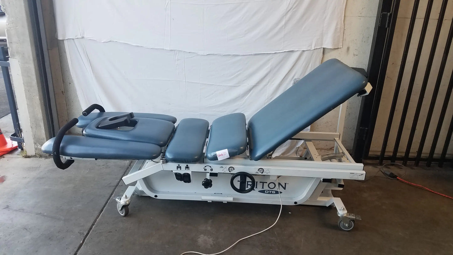 Blue padded adjustable triton dts table with white metal frame and casters for physical therapy equipment use