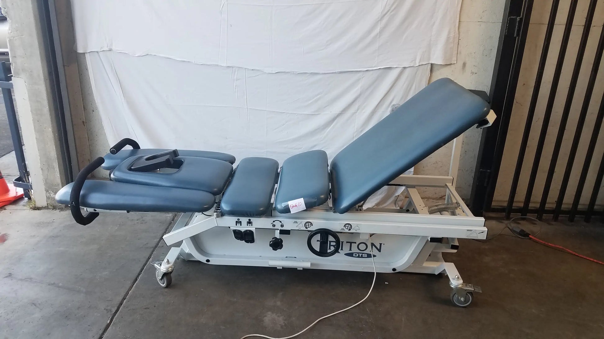 Blue padded adjustable triton dts table with white metal frame and casters for physical therapy equipment use