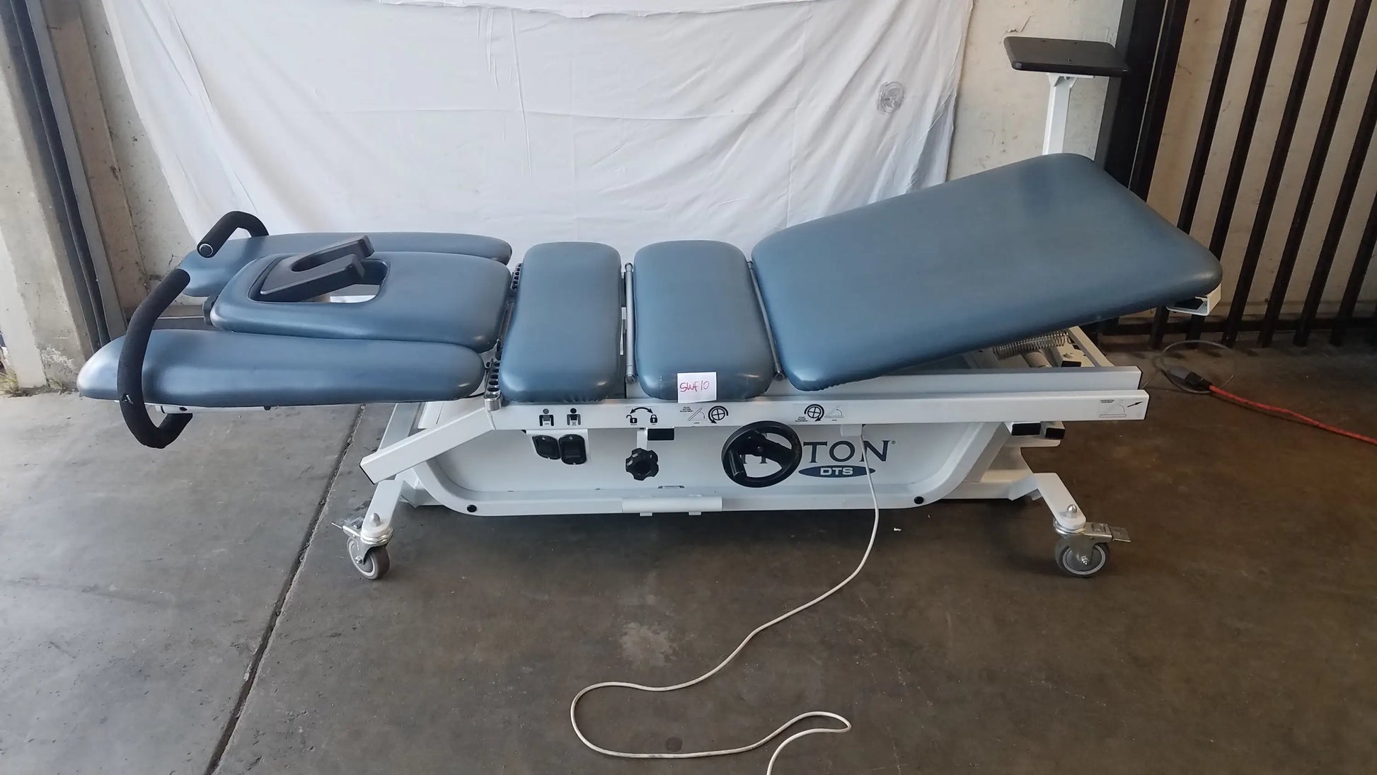 Blue padded adjustable triton dts table with white metal frame and casters for physical therapy equipment use
