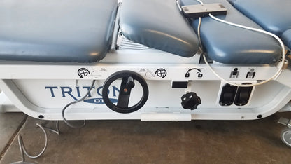 White triton dts adjustable medical treatment table with gray padded sections and black control knobs for physical therapy equipment