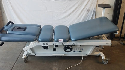 Gray upholstered adjustable Chattanooga Triton DTS traction table with white metal frame and casters for physical therapy equipment