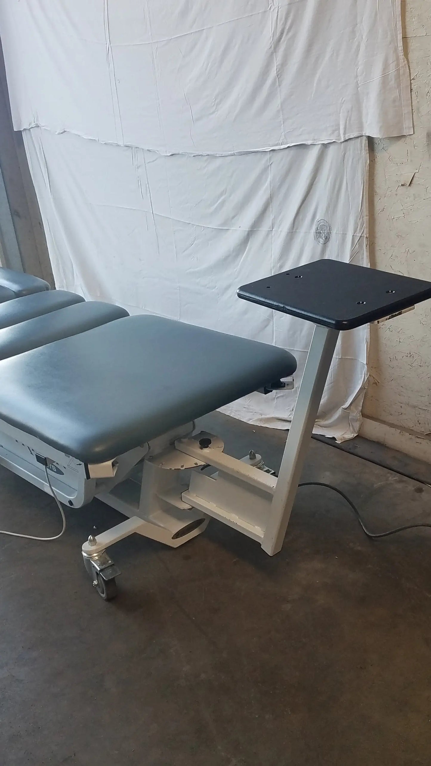 Gray upholstered adjustable Chattanooga TRT-600 Triton DTS table with black side tray and white metal frame for physical therapy equipment