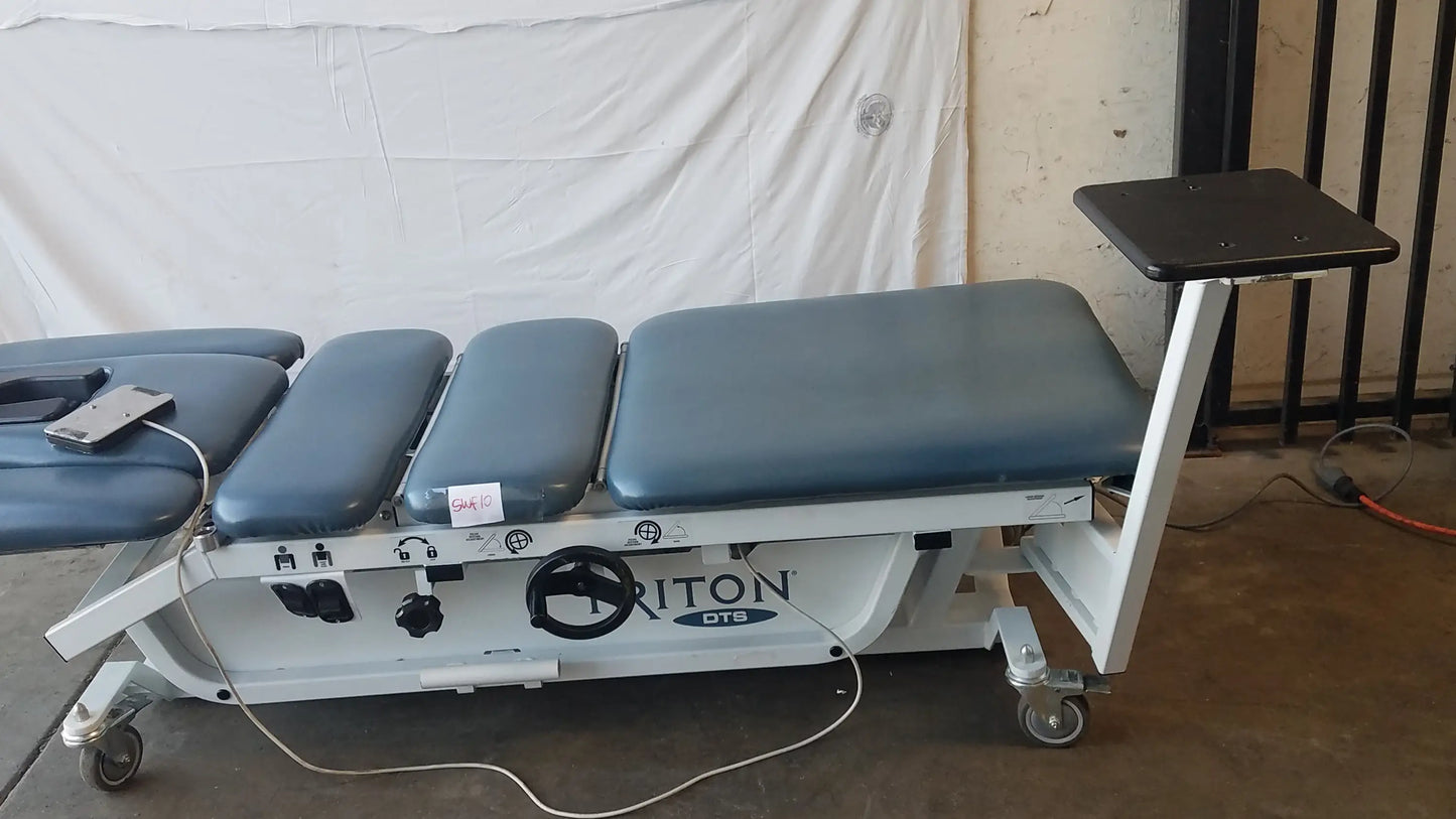 Gray padded adjustable triton dts table with white metal frame and casters for physical therapy equipment use