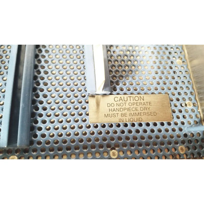 Brass warning plaque with engraved black text on the back of cooper vision 390 unipak handpiece for safe reuse medical handling