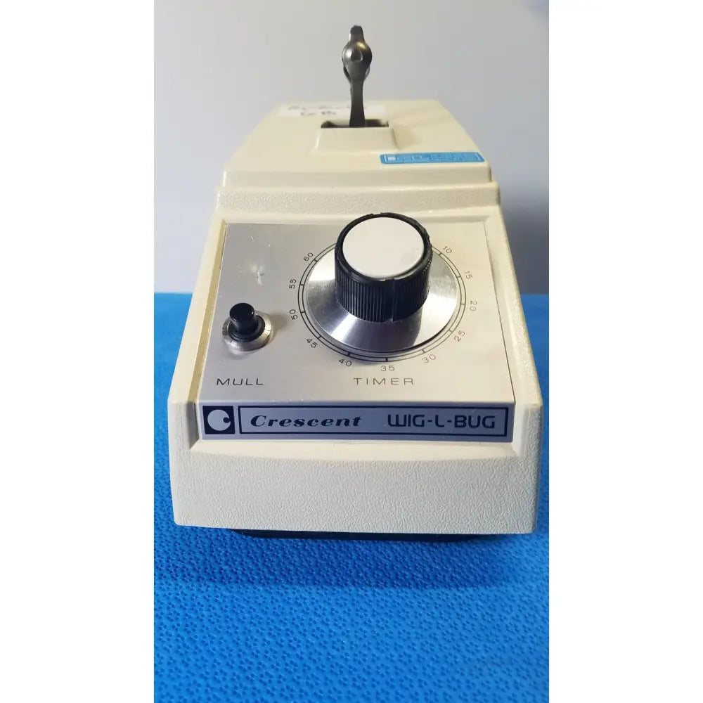 Cream-colored crescent dental wig-l-bug amalgamator with black rotary timer dial and metallic handle for laboratory use