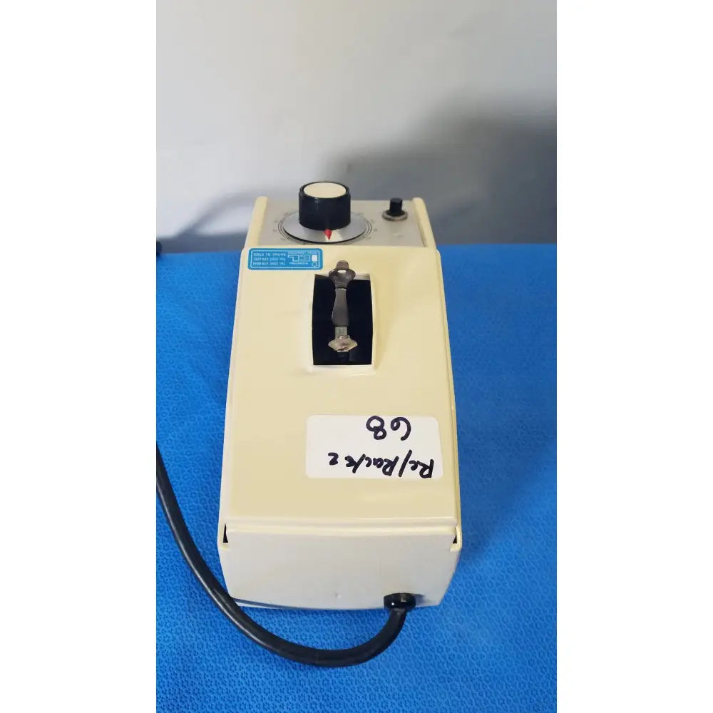 Cream-colored plastic crescent dental wig-l-bug dental amalgamator with black rotary knob and metal key slot labeled re back 2