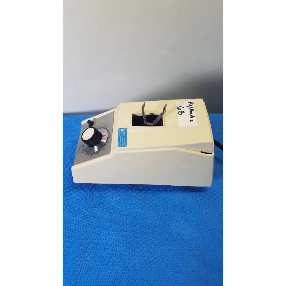 Cream-colored crescent dental wig-l-bug amalgamator with black rotary knob and metallic clamps for dental use
