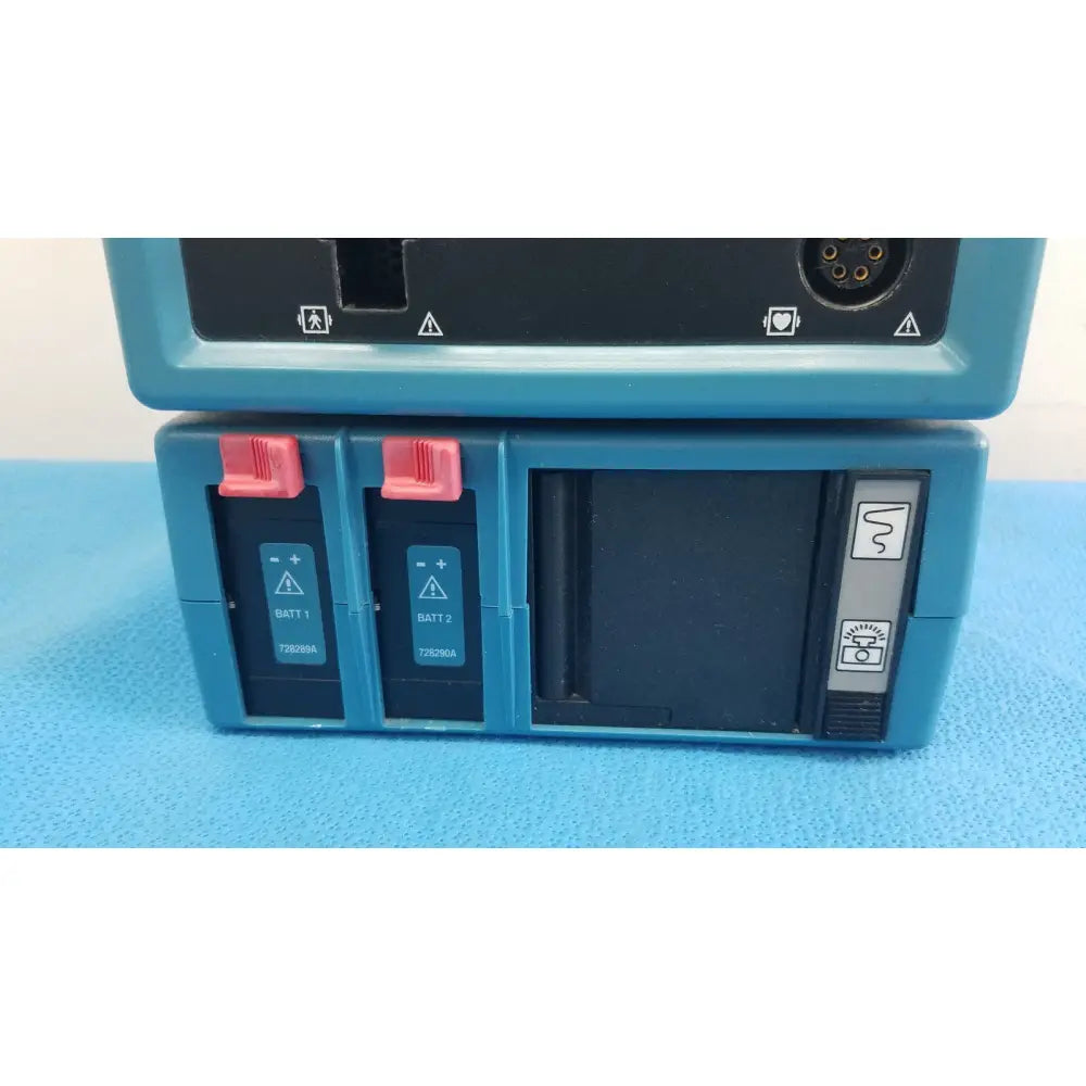 Backside of blue critikon dinamap plus vital signs monitor 8726 with two red batt compartments and warning symbols