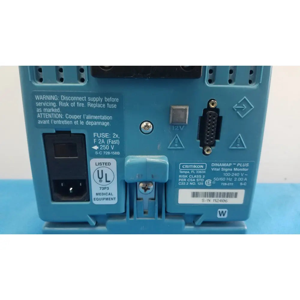 Blue plastic back panel of critikon dinamap plus vital signs monitor with labeled ports fuse slot and safety warnings