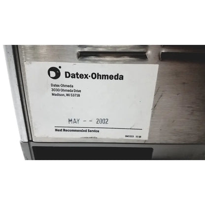 A white label with black text and logo on a metallic surface of the datex ohmeda tec 6 desflurane anesthesia vaporizer
