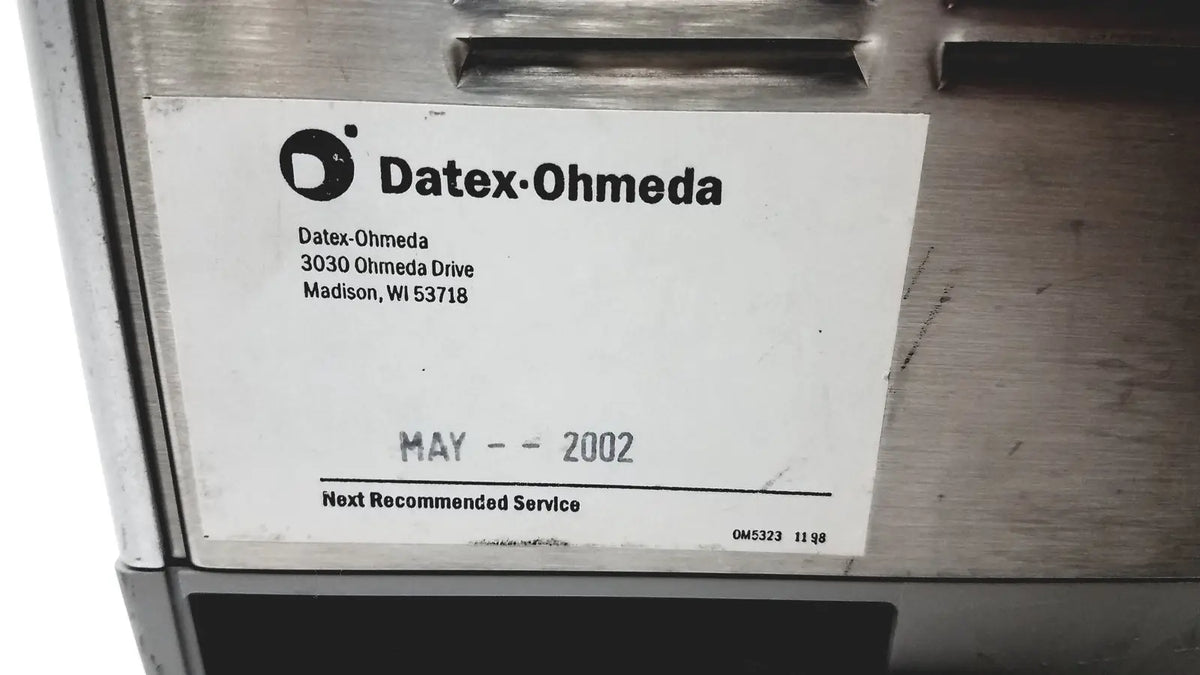 A white label with black text and logo on a metallic surface of the datex ohmeda tec 6 desflurane anesthesia vaporizer