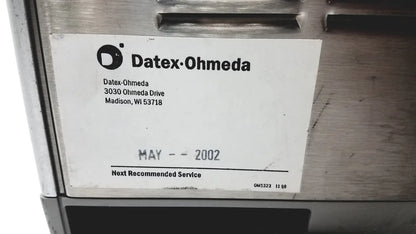 A white label with black text and logo on a metallic surface of the datex ohmeda tec 6 desflurane anesthesia vaporizer